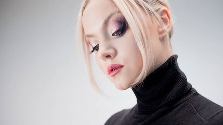 Portrait of a stylish strict blonde in a black turtleneck with stylish eye makeup, white backgroundの写真素材
