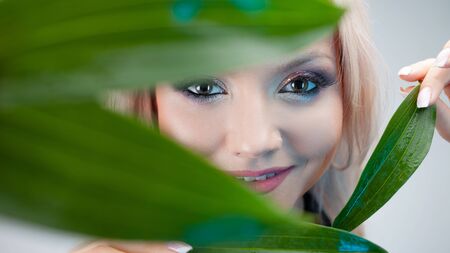 Natural cosmetics, concept. Charming blonde makes the petals of the plant to the eyes, as eyes patchesの写真素材