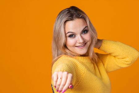 Happy and cheerful blonde in a yellow sweater on a yellow background. Positive young woman rejoices and dances, portrait close-up. copy spaceの写真素材