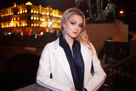 Stylish and elegant young woman in a beige coat on the city waterfront. Night city in autumn.の写真素材