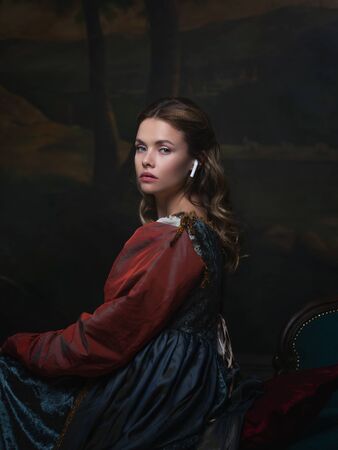 Old and new, concept. Portrait of a girl with a wireless earphone. Beautiful young Renaissance style...