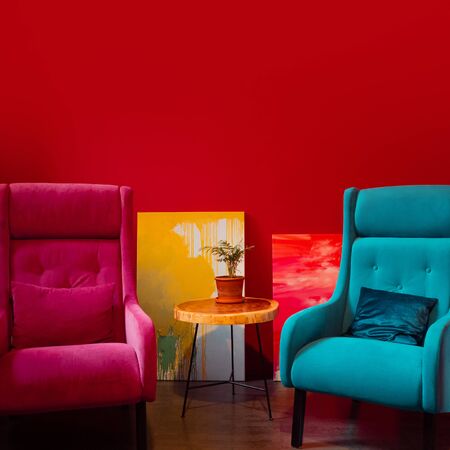 Two bright chairs opposite each other. A dialogue between two opponents, the concept. A blue and pink armchair against a red wallの写真素材