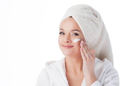 Portrait of a young attractive woman in a Bathrobe and a towel on her head. girl uses a cream and face mask.の写真素材