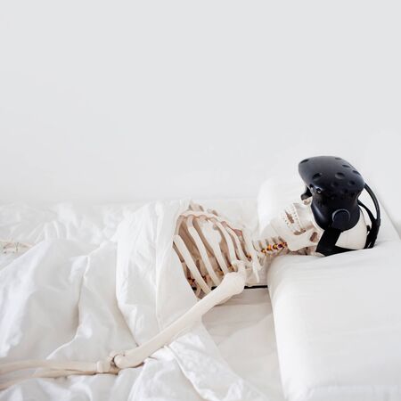 Gamer became interested in a computer game and died. A human skeleton in a VR helmet, lying in a white room on a bed.の写真素材