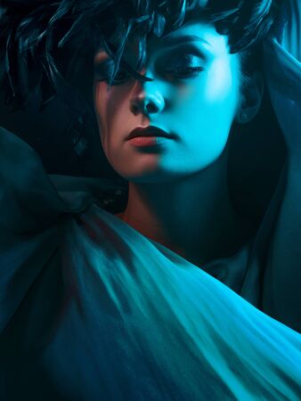 Beautiful young woman in mysterious emerald light. Hat of black feathers, fashion and the image of the luxury make-upの写真素材