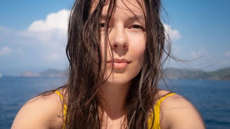 Vacation at the sea, young woman with wet hair after swimming, close-up portrait. Portrait on the background of the sea, the bright sunの写真素材