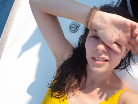 young woman in a bright yellow one-piece swimsuit sunbathing on the deck of a sailing yacht. Holidays at the seaside, sunburn and sun protectionの写真素材