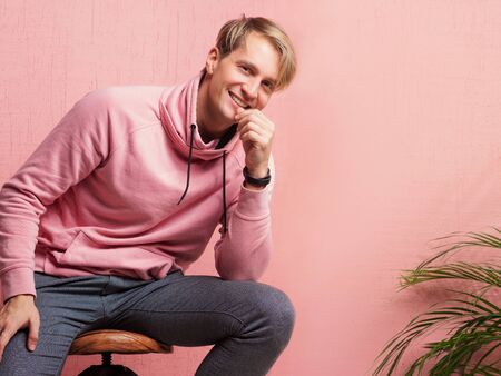 Positive guy in coral hoodie on pink background. Happy and smiling young man in casual clothes looks at the camera, portrait with real emotionsの写真素材