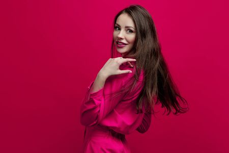 Cute and cheerful young brunette in a pink suit on a pink background. Positive young woman in a bright image in crimson shadesの写真素材