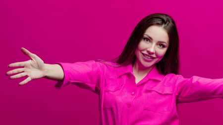 Cute and cheerful young brunette in a pink suit on a pink background. Positive young woman in a bright image in crimson shadesの写真素材