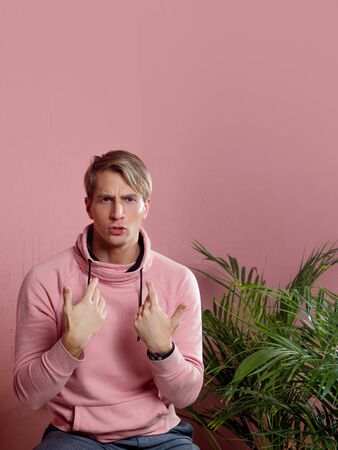 Positive guy in coral hoodie on pink background. Conversation and gestures, pointing the finger at yourselfの写真素材