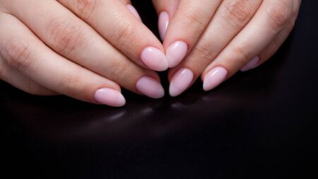 Women's hands with perfect manicure. Nail Polish is a natural pale pink shade. Black background, close-upの写真素材