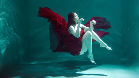 beautiful girl in a red dress swims under water. amazing Underwater beauty photo.の写真素材