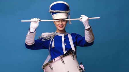 Charming cheerful drummer in a blue uniform, sings and plays the drum. Blue background copy space