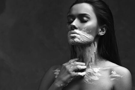 Dumbness and inability to speak about problems and thoughts, psychology. Portrait of a young beautiful woman with paint or clay on her face, shut up and close her mouth. Sad black and white portraitの写真素材