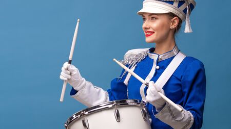Charming cheerful drummer in a blue uniform, sings and plays the drum. Blue background copy space