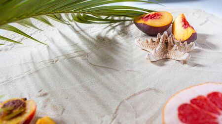 Beach vacation. A palm leaf, a starfish, and a white tree branch and juicy fruits lie on white fine sand. Close-up, top view, desktop wallpaper. Copyspace.の写真素材