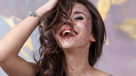 Sequins in makeup, a fashionable youth trend. Beautiful young girl happy and laughing, portrait in the Studioの写真素材