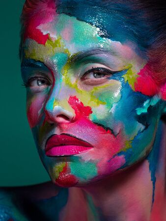 Face art and body art. Creative makeup with colorful patterns on the face. Modern makeup art, bold style, close-up portrait of a womanの写真素材