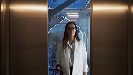 Charming young business lady in the Elevator in the business center. A young woman in a white jacket...