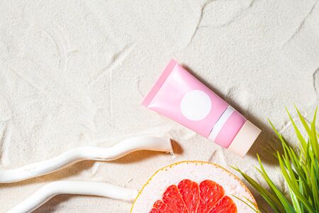 Safe sun. Skin care. A tube of cream lies on the beach sand, surrounded by vibrant fruits, corals, and palm leaves. Close-up, top view, desktop wallpaper. Copyspace.の写真素材