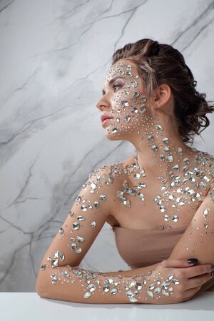 fabulous fashion portrait of a young beautiful woman with transparent crystals on her face and shoulders. An unusual image on a marble backgroundの写真素材