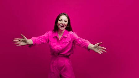 Cute and cheerful young brunette in a pink suit on a pink background. Positive young woman in a bright image, copy spaceの写真素材