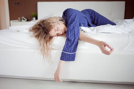 Too lazy to get out of bed, Woman in blue pajamas lying in bed and does not want to get up,...