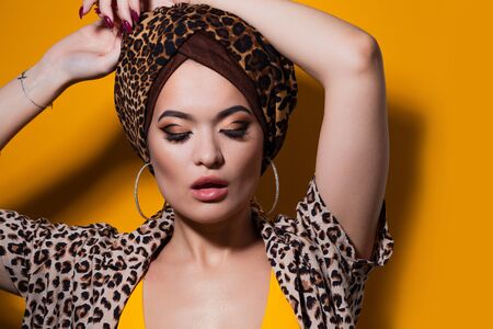 Bold and beautiful young woman in a turban with a leopard print, ethnic trends, portrait on a bright yellow backgroundの写真素材