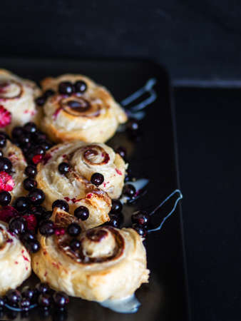 Cinnamon rolls with raspberries and blackcurrant, delicious homemade cakes dark backgroundの写真素材
