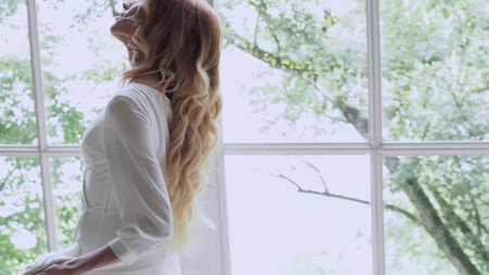 Beautiful elegant bride in a simple white wedding dress with sleeves on the window backgroundの写真素材