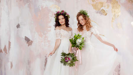 Two charming brides in beautiful spring wreaths on their heads. Beautiful young women in wedding dresses, Studio portraitの写真素材