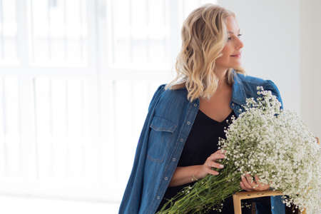Stylish young blonde woman with a bouquet of gypsophila. Portrait in the interior. Happy Girl with a...