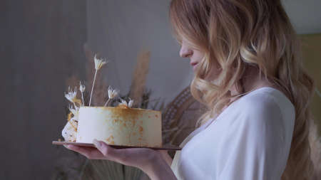 Beautiful elegant bride in a simple white wedding dress with sleeves holding a small wedding cakeの写真素材