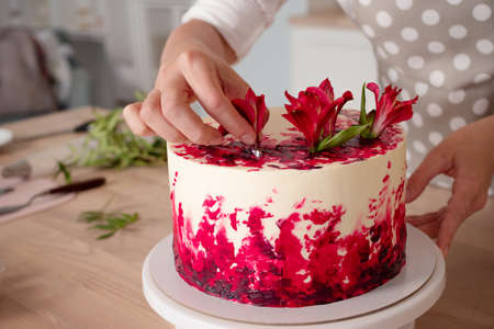 cooking and decoration of cake with cream. Young woman pastry chef in the kitchen decorating red...