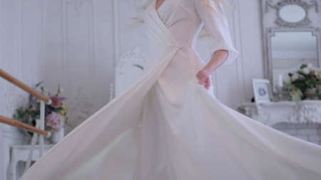 Beautiful elegant bride in a simple white wedding dress with sleeves, dancing and twirling in a dressの写真素材