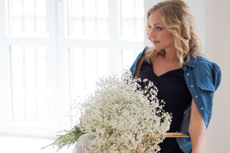 Stylish young blonde woman with a bouquet of gypsophila. Portrait in the interior. Happy woman with a bouquet of flowers, flower deliveryの写真素材