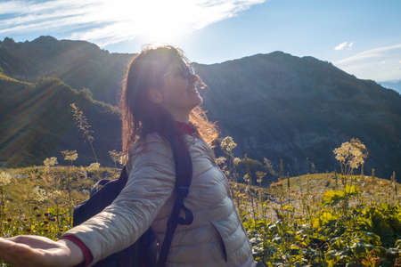 Happy young woman on nature in the mountains, sun rays and glare. A tourist in a backpack in the...