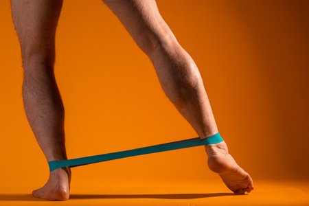 Muscular mens legs with elastic band for fitness, do exercises to strain the leg muscles. Body Parts, yellow backgroundの写真素材