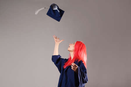 Happy graduate on a gray background. A young woman with bright hair