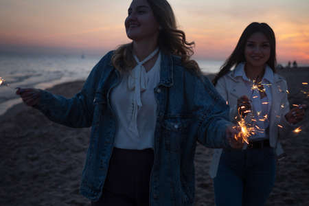 Two cheerful friends on the beach in the evening light sparklers.の写真素材
