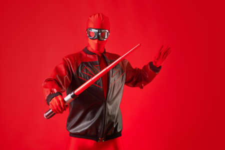 Funny super hero in a red leotard and protective glasses uses a toy sword.