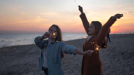 Two young women with sparklers in the open air. Friends having fun on the beach,