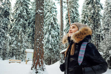 young woman in a winter down jacket with fur hood walks in the forest in winterの写真素材