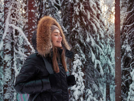 young woman in a winter down jacket with fur hood walks in the forest in winterの写真素材