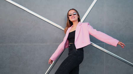 A young stylish woman in a fashionable pink jacket and sunglasses