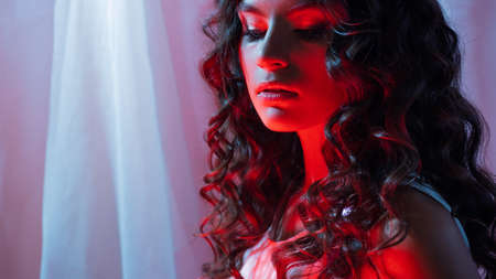 Beautiful young brunette with curly hair, portrait in neon light, bright redの写真素材