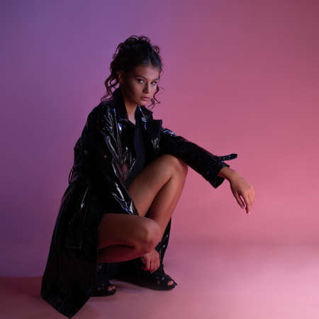 Stylish young brunette in a latex raincoat over a black bodysuit,の写真素材