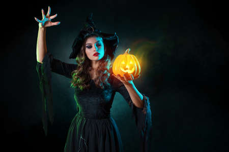beautiful witch with a hat conjures over jack-o-lantern pumpkin.の写真素材
