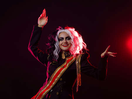 A bright and shocking woman with a black and white hairstyle is dressed in a decorated uniform and a full skirt. Red backlight at the back. waves a handの写真素材